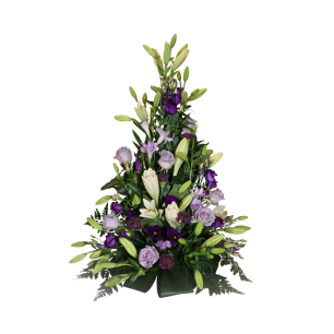 En blomsterarrangemang i pyramidform med vita liljor och lila blommor, omgivna av gröna blad.